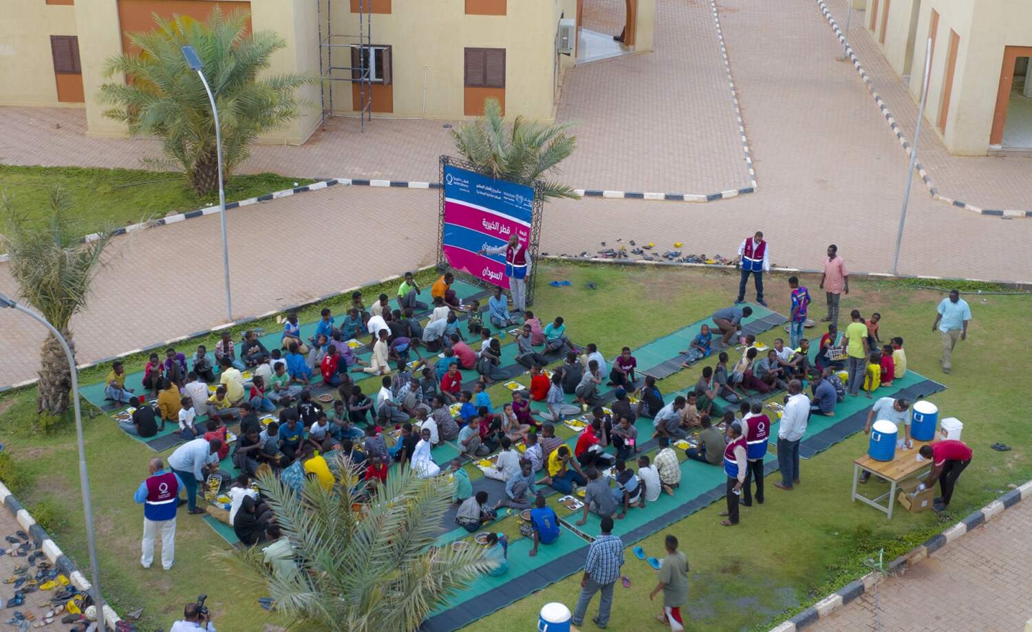 Qatar Charity staff serve a shared meal to children on the lawn of an orphan residential complex