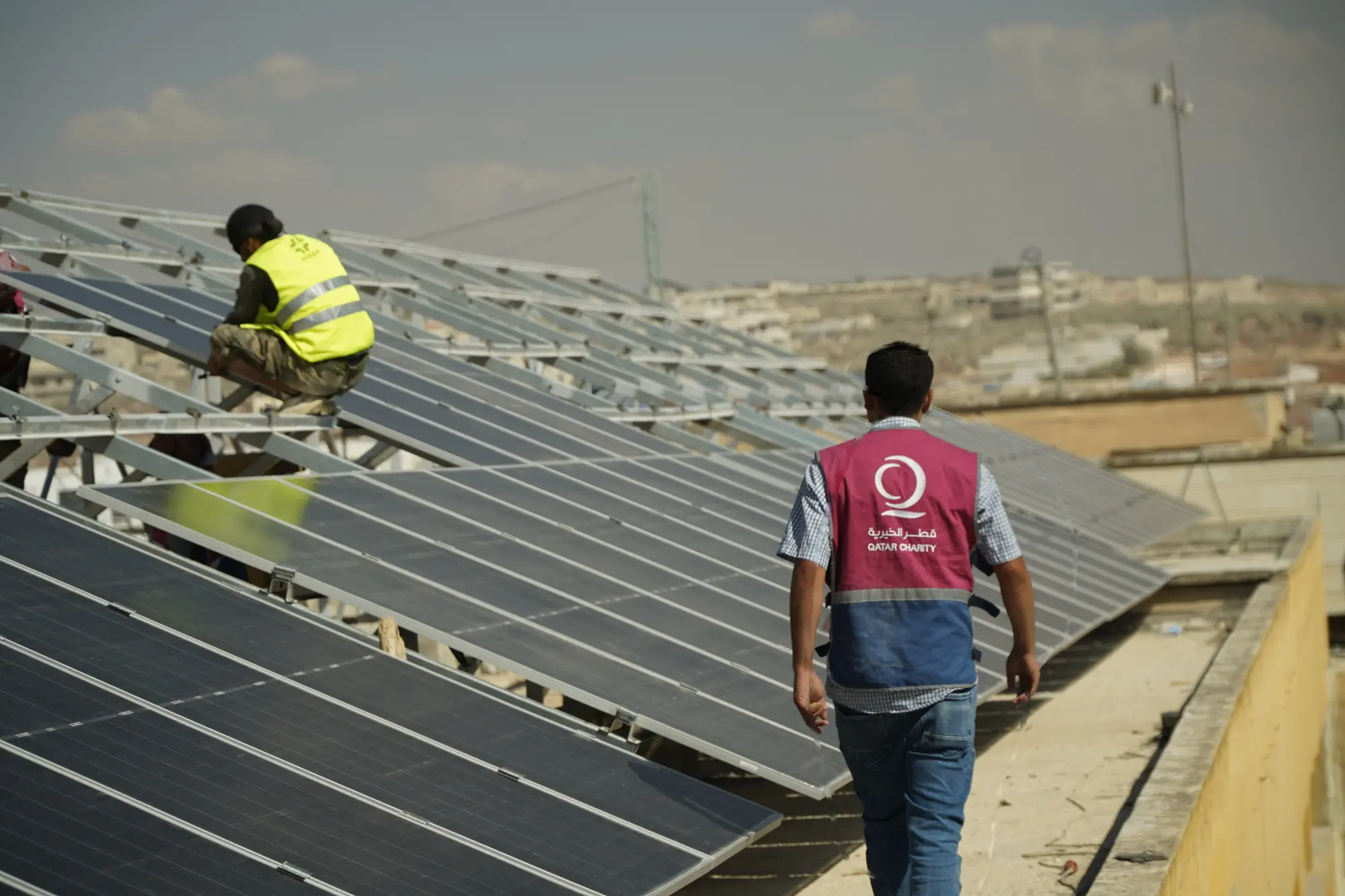 عامل من قطر الخيرية يمر بجانب ألواح شمسية أثناء تركيبها على سطح مبنى